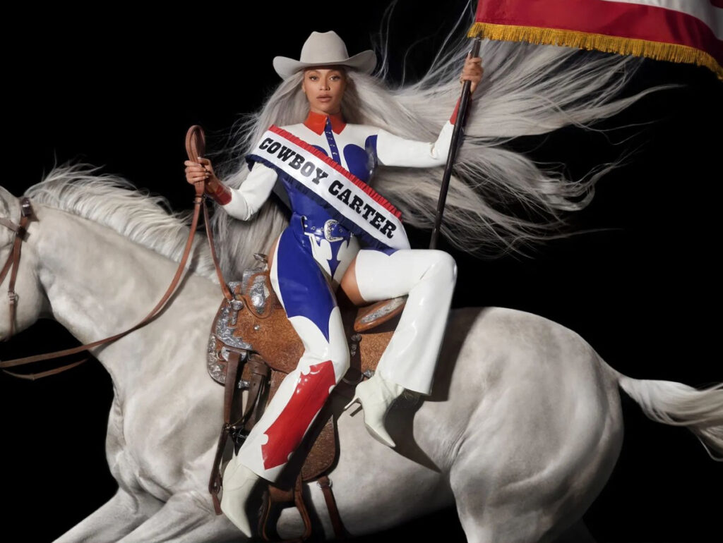 Beyoncé - Imagem de uma mulher montada em um cavalo, vestindo um traje estiloso e segurando uma bandeira, simbolizando o tema Cowboy Carter.