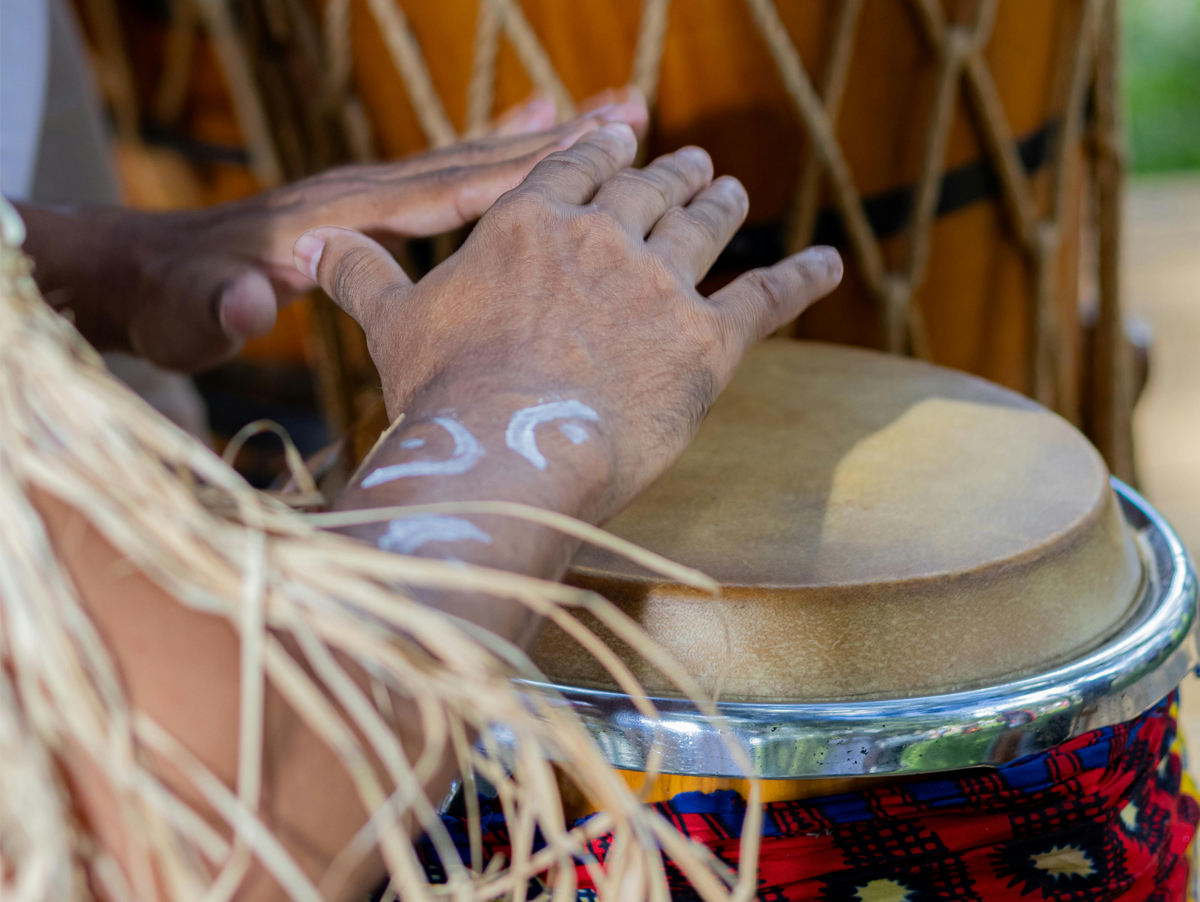 Imagem de uma mão tocando um tambor, destacando os detalhados traços brancos na pele e a textura do tambor sob uma luz natural.