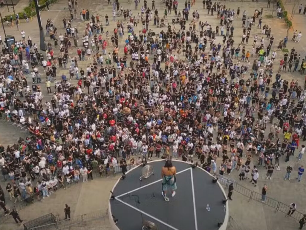 Matuê - Imagem aérea de um grande público reunido em torno de um palco, com uma performance ao vivo no centro, destacando a energia e emoção do evento.