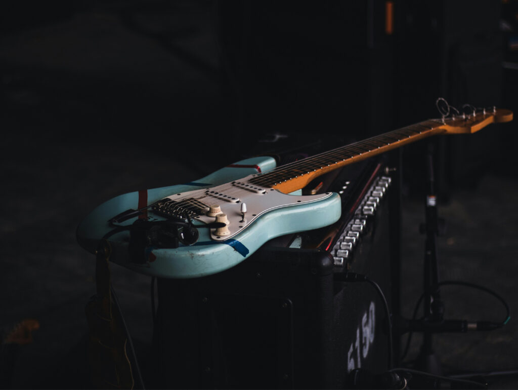 Imagem de uma guitarra elétrica azul repousando sobre um amplificador, destacando seu design e detalhes sonoros, ideal para amantes da música.