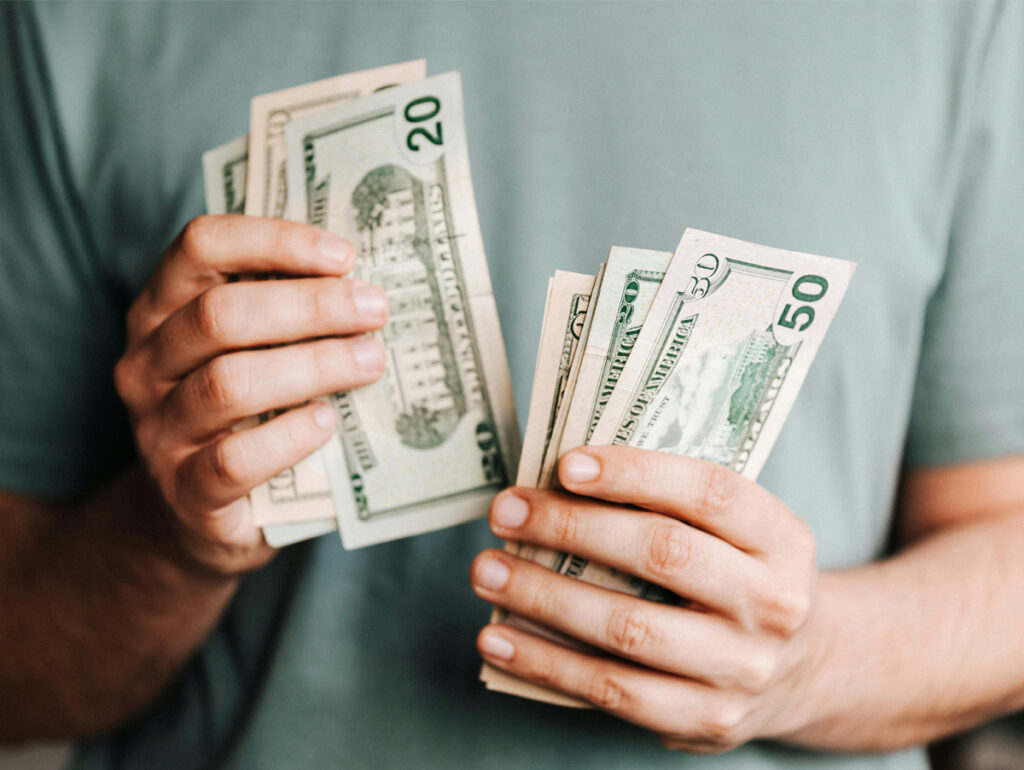Investimentos no mercado da música - Uma pessoa segurando diversas notas de dólar, incluindo valores de 20 e 50, ilustrando a gestão financeira e a importância do dinheiro.