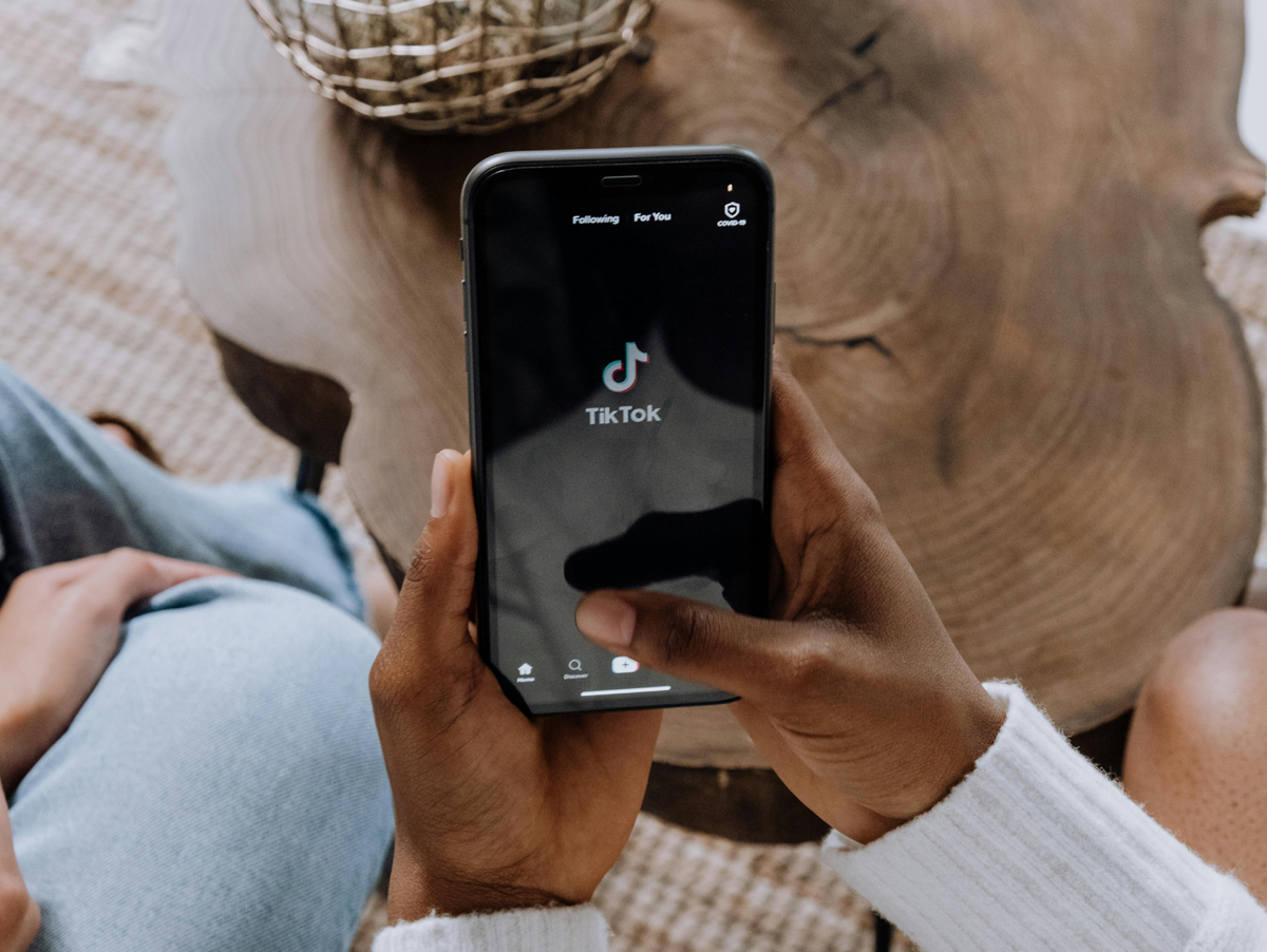 Usuário acessando o aplicativo TikTok em um smartphone, destacando a interface do app com a logo do TikTok. O cenário apresenta um ambiente confortável e aconchegante. Estudo da Luminate avalia o impacto do app.